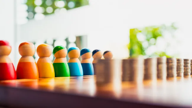 Colorful wooden figures lined up in front of coin stacks